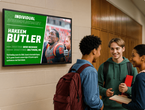 3 students standing in front of school digital signage showing a hall of fame display
